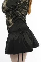 Minifalda negra de tafeta con cintura alta elastizada, diseño con volado y lazos laterales ajustables.