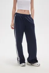 Pantalon deportivo de corte recto y tiro medio, color tostado, con cintura elástica y franjas laterales en tono más claro. Presenta aberturas en los tobillos con cordones ajustables.