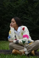 Cardigan de lana merino tejida a mano con dos agujas, color blanco con diseño de figuras geométricas en tonos multicolor y cierre frontal con botones de madera.