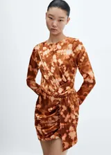 Vestido corto de manga larga con diseño drapeado y cruzado en la cintura. Presenta cuello redondo y un estampado tie-dye en tonos marrones y beige sobre un tejido satinado y fluido.