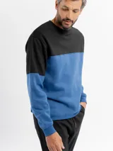 Buzo de felpa con diseño de bloques de color, combinando negro en la parte superior y azul en la parte inferior y mangas. Presenta cuello redondo y puños elásticos.
