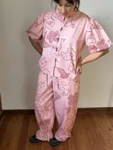 Camisa de popelina de algodón con cuello mao, botones frontales agrupados en pares y mangas cortas abullonadas tipo balloon. Cuenta con un diseño estampado de patrón geométrico y floral sobre fondo negro.