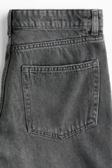 Jean de corte baggy, estilo holgado con piernas rectas, confeccionado en denim de algodón color gris oscuro con efecto lavado. Cuenta con tiro estándar, trabillas para cinto, cierre frontal con botón y cinco bolsillos clásicos.