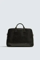Bolso de viaje de diseño rectangular con acabado craquelado en tono oscuro. Cuenta con doble asa de mano, compartimento principal con cierre de cremallera, bolsillo interior con cierre y correa de hombro ajustable y extraíble.