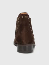 Bota corta tipo chelsea de gamuza color marrón, con detalle de tachas metálicas doradas a lo largo del elástico lateral y tacón bajo cuadrado.