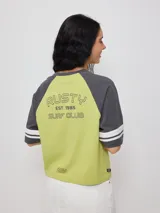 Remera bicolor Rusty con cuerpo verde lima y mangas ranglán grises con dos rayas blancas en los puños. Estampado frontal con el logo de la marca y el número 85.