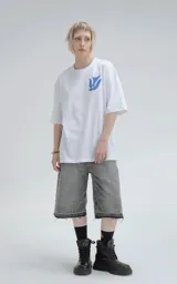 Remera blanca de corte holgado con estampa central en color azul que combina motivos geométricos tipo chakana con figuras de aves dispuestas en círculo.