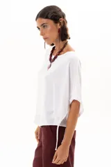 Blusa blanca de corte holgado y diseño minimalista, con mangas cortas tipo murciélago que presentan un detalle de fruncido lateral con cordón ajustable.