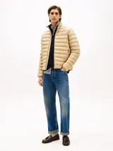 Campera acolchada de corte amplio, color beige, con cuello levantado y cierre de cremallera. Presenta dos bolsillos laterales ribeteados con cremallera y el logo de Tommy Hilfiger bordado en el pecho.