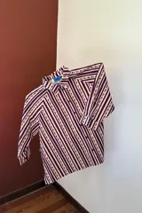 Camisa de manga larga con cuello clásico y cierre frontal de botones. Presenta un diseño de rayas verticales verdes y blancas con un estampado lineal de pequeñas flores rojas.