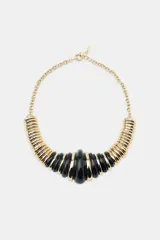Collar tipo babero o gargantilla con cadena dorada y secciones de piezas acrílicas negras y doradas, con forma de tubo acanalado y centro abultado.