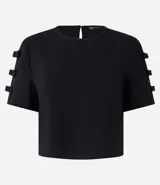 Blusa negra de crepé con cuello redondo y mangas cortas decoradas con lazos aplicados.