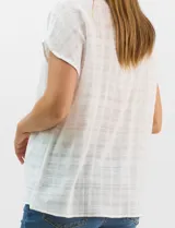 Blusa de corte fluido confeccionada en algodón con tejido texturizado de patrón a cuadros. Presenta mangas cortas caídas, escote redondo y cierre frontal con botones.