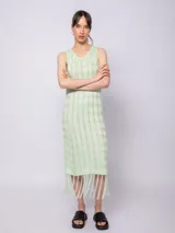 Vestido largo tejido de punto color verde claro, sin mangas, con diseño de tramado calado y flecos en el ruedo.