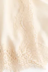 Top de seda color beige con escote recto, breteles finos ajustables, detalles de alforzas verticales en el centro y ribetes de encaje en los laterales y en el bajo festoneado.
