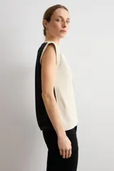 Remera sin mangas de corte recto, confeccionada en dos tonos, con frente en color beige claro con escote en V y espalda en color negro. Cuenta con detalle de botones en los laterales.