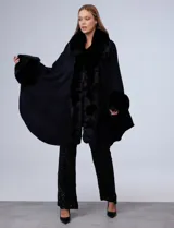 Ruana de tejido color tostado con cuello, bordes frontales y puños amplios con apliques de piel sintética al tono. Presenta una abertura central con cierre de botón tipo trenca.