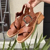 Sandalias de cuero vacuno color suela, con diseño de tiras cruzadas en el empeine y hebilla metálica lateral. Presentan punta cuadrada y taco de madera de 5 cm.