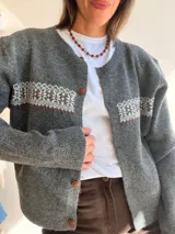 Cárdigan de punto azul marino con diseño jacquard en la parte superior del pecho. Presenta cuello redondo, cierre frontal con botones marrones y puños y ruedo acanalados.