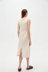 Vestido midi de viscosa color beige, sin mangas y con cuello a la base. Presenta una abertura frontal con botones decorativos y detalles de frunces en el centro del pecho.