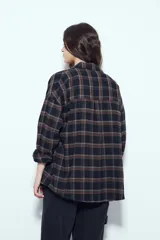 Camisa tipo leñadora de corte oversize, con estampado de cuadros en tonos negro y marrón. Presenta cuello clásico, cierre frontal con botones y mangas largas con puños abotonados.