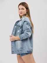 Campera de jean celeste con detalles de roturas, corte oversize, cuello clásico, cierre con botones metálicos, bolsillos frontales con solapa y puños abotonados.