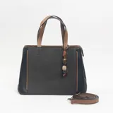 Cartera tipo tote de diseño estructurado, combinando paneles de tela gris oscuro con laterales y detalles en cuero sintético negro y marrón. Incluye doble asa superior, correa larga ajustable y extraíble, y un dije decorativo con cuentas de madera y piedra.
