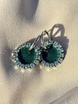 Aros colgantes con forma circular, hechos de resina color lila y borde de strass plateado. El aro es de acero quirúrgico plateado.