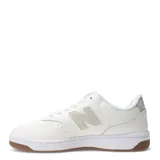 Championes urbanos New Balance de diseño minimalista, color blanco con detalles en tono crema. Presentan el logo N característico en el lateral, suela blanca con base de goma color caramelo y cierre mediante cordones.