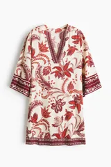 Vestido túnica corto en tejido de viscosa, de corte oversized con hombros caídos y mangas tres cuartos. Presenta escote en V tanto en la parte delantera como en la trasera, con detalles de cenefas estampadas en contraste en el escote, los puños y el ruedo.