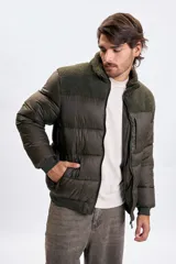 Campera puffer color verde oliva oscuro con diseño capitoneado. Presenta un panel superior en tejido tipo corderito en el pecho y cuello alto. Cuenta con cierre frontal completo, puños y cintura elástica acanalada, y un bolsillo vertical con cierre en el pecho.