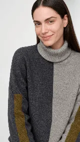 Polera de cuello alto confeccionada en lana lambswool, con diseño bicolor en negro y marrón. Presenta mangas largas con franjas verticales en gris y un parche circular bordado en la manga derecha.