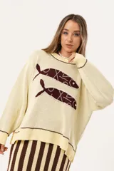 Sweater color manteca de tejido de punto con cuello redondo y ribete marrón. Presenta dos peces marrones tejidos en el frente con detalles bordados a mano.