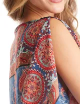 Blusa de gasa con estampado de arabescos en tonos azules y rojos, con cuello a la base y mangas tipo capa. Presenta una silueta holgada con ruedo elástico en punto smock que ajusta a la cintura.