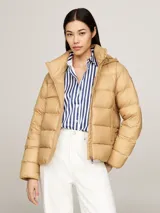 Campera puffer color beige, con capucha y cierre frontal con cremallera. Tiene dos bolsillos delanteros con botón a presión y parche con el logo de Tommy Hilfiger en la manga.