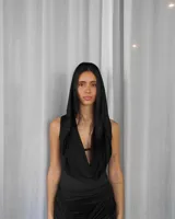 Body negro con escote drapeado, mangas cortas y falda larga con tajo alto y abertura en la cintura.