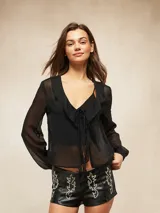 Blusa negra de tela semitransparente con escote en V, volados en el frente y cierre de lazo. Posee mangas largas con puños ajustados.