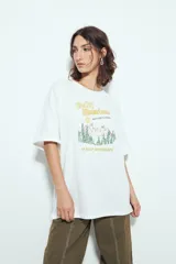 Remera blanca de manga corta con calce relajado y cuello a la base. Presenta un estampado frontal pequeño y una estampa protagonista en la espalda con el texto "Rocky Mountain National Park" y un paisaje de montañas y árboles.