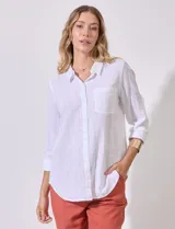 Camisa blanca de corte clásico con textura de líneas verticales, cuello con solapa, cierre frontal con botones y bolsillo en el pecho. Presenta mangas tres cuartos regulables con presilla y botón.