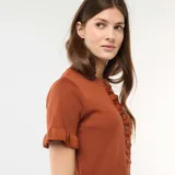 Camiseta de punto color marrón, de manga corta con terminación en volantes, cuello redondo y cierre frontal con botones, decorada con una hilera de volantes a lo largo de la botonadura.