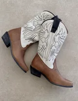 Botas de cuero color marrón y blanco con bordados negros, de estilo cowboy con taco bajo.