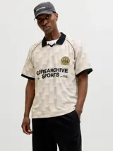 Camiseta tipo polo de manga corta con calce suelto. Presenta un diseño de cuadros en tonos beige y crema, con cuello y bordes de mangas en color negro. Incluye un escudo circular bordado en el pecho y estampado tipográfico en el frente.