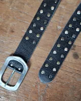 Cinto de cuero marrón con hebilla metálica de estilo envejecido y detalle de tachas metálicas en diferentes tonos en el extremo.