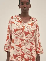 Camisa de manga 3/4 confeccionada en seda viscosa con un diseño estampado de flores y tigres en tono terracota. Presenta cuello camisero, cierre frontal con botones y un calce fluido.