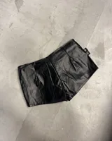 Shorts negros de efecto cuero con doble cinturón incorporado, con múltiples hebillas cuadradas plateadas y ojales metálicos.