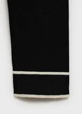Jersey de punto fino en color negro con cuello de pico y mangas largas. Presenta detalles de líneas blancas en contraste en el borde del cuello y en los puños.
