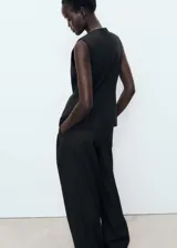 Chaleco sastrero negro sin mangas, con cuello redondo, tirantes anchos, diseño recto y cierre delantero con botones.