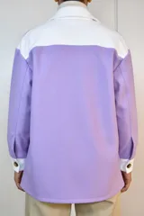 Sobre camisa de corte holgado en combinación de colores lila y blanco. Presenta cuello clásico, cierre frontal con botones, dos bolsillos frontales con solapa y puños en contraste.