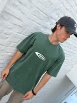 Remera de manga corta color verde oscuro con efecto acid wash y un logo ovalado blanco con el texto "OSTEN" en el centro del pecho.