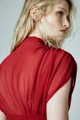 Vestido corto de color rojo confeccionado en tejido mesh. Presenta cuello subido, diseño sin mangas con frunces en los hombros y falda con drapeado lateral. Incluye cierre lateral con cremallera oculta.
